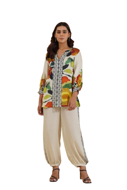 Woman wearing a floral patterned tunic with decorative trim and light-colored pants.